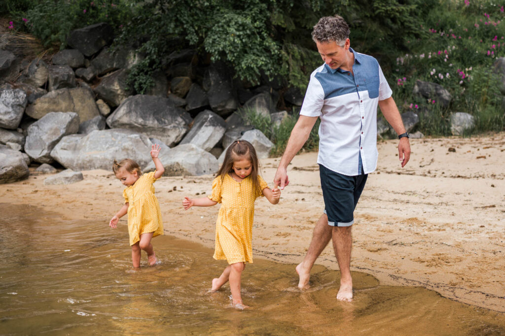 Dad and daughters walking along a beach at the precise moment when they all look like they're practicing dance moves.